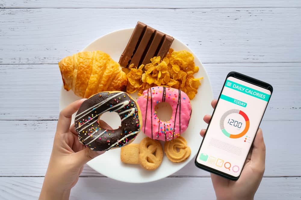 person holding a donut and phone showing calories counting app